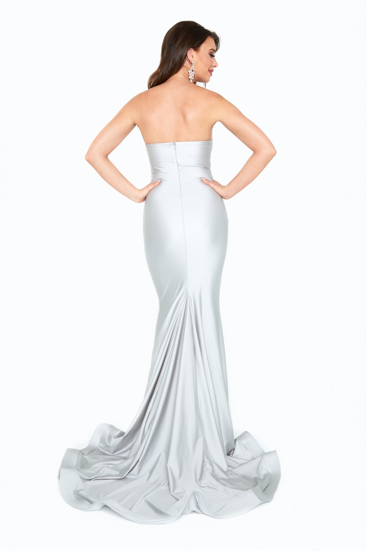 Woman in a silver Ruched-Waist Strapless Long Prom Dress (6538H), floor-length with a slight train, stands with hands on hips and faces away from the camera.